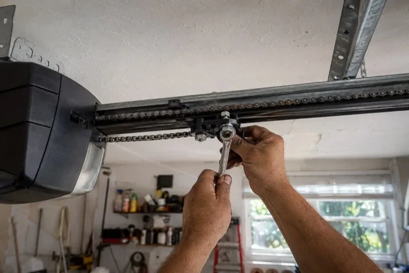 Hands holding a wrench against an opener trolley beneath a chain rail — Chain-Drive Opener Repair, Brant
