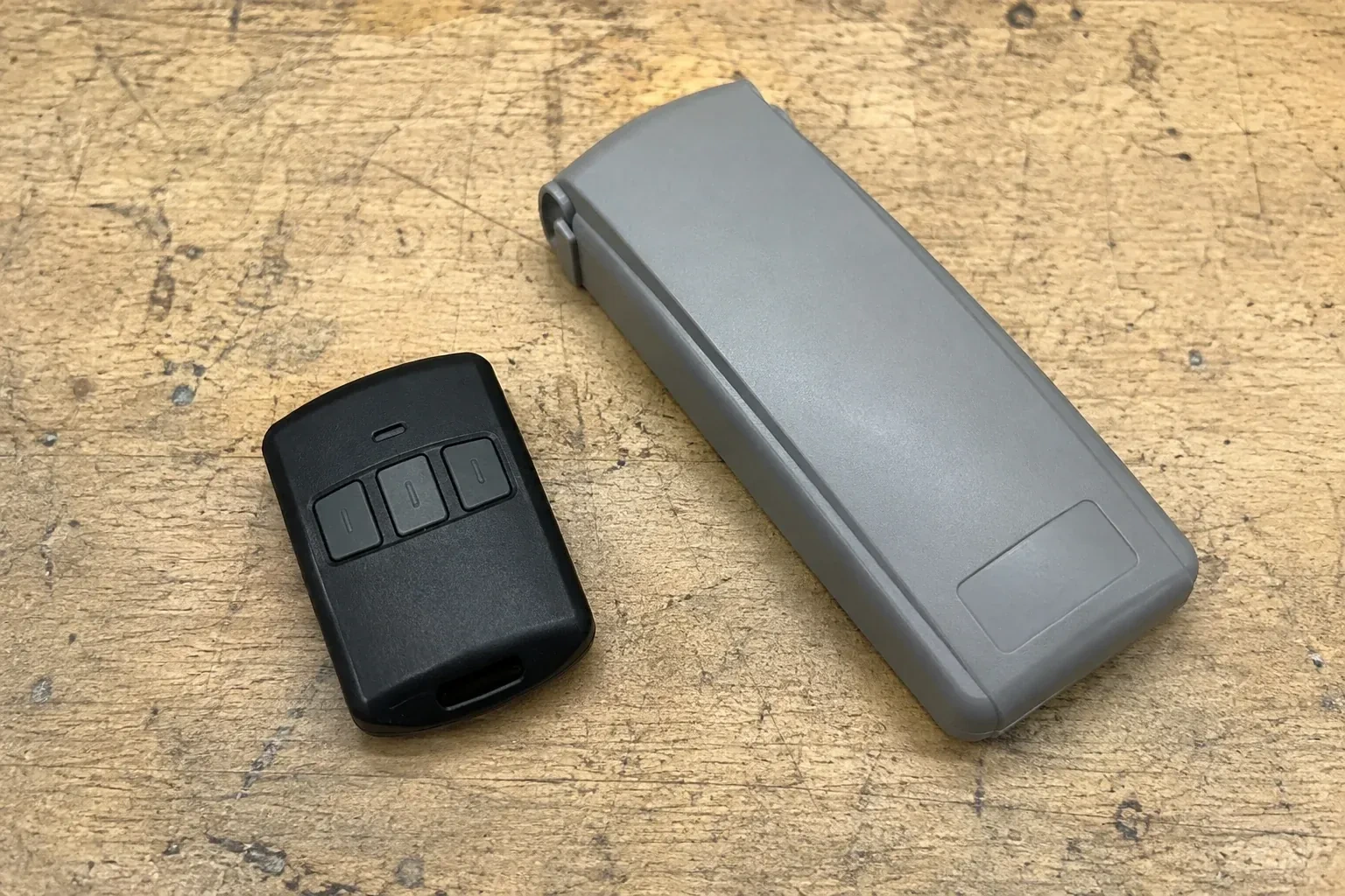 Three-button remote beside a closed grey keypad cover on a workbench. — Garage Door Remote and Keypad Programming, Brant