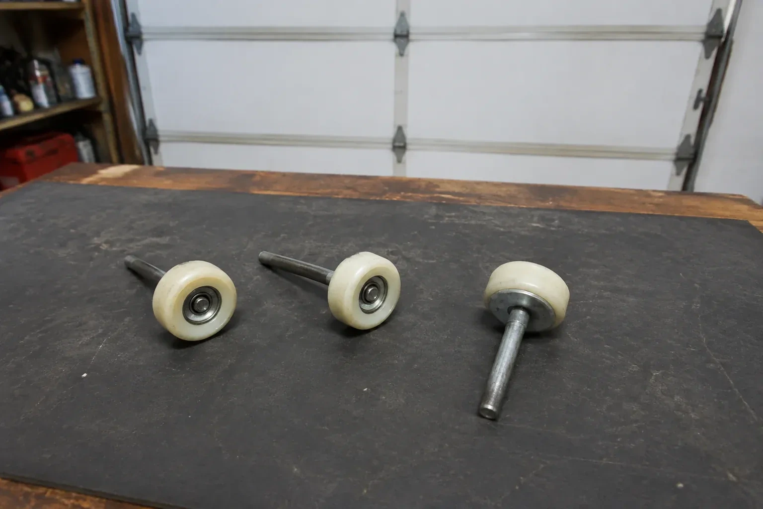 Three detached nylon-wheel garage door rollers with steel stems on a work mat. — Garage Door Roller Replacement, Brant